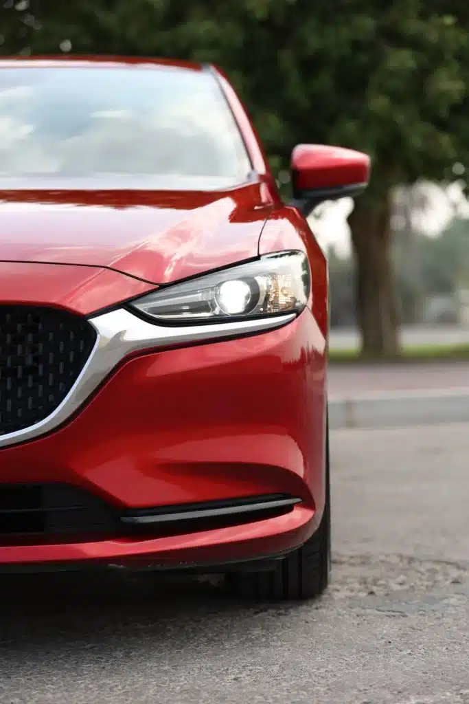 Voiture Rouge Vif : Détail des Phares LED de la Mazda 6 Détail de l'avant d'une Mazda berline rouge vif. Le phare LED est allumé, soulignant la calandre noire et la finition chromée du design.